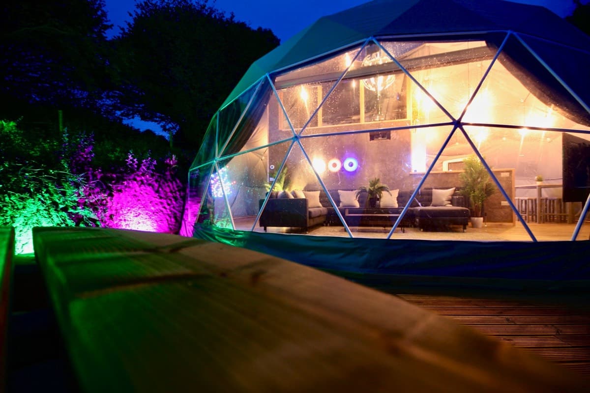 Cozy and unique geodome accommodation at Sunridge Retreats, lit up at night with warm interior lighting visible through the window