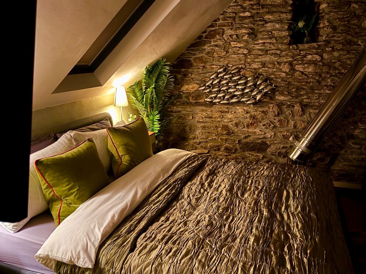 Cosy bedroom with green throw and rustic stone feature wall.
