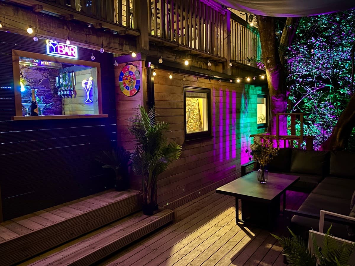 Intimate evening setting at the lower deck bar, enhanced by ambient lighting and forest sounds.